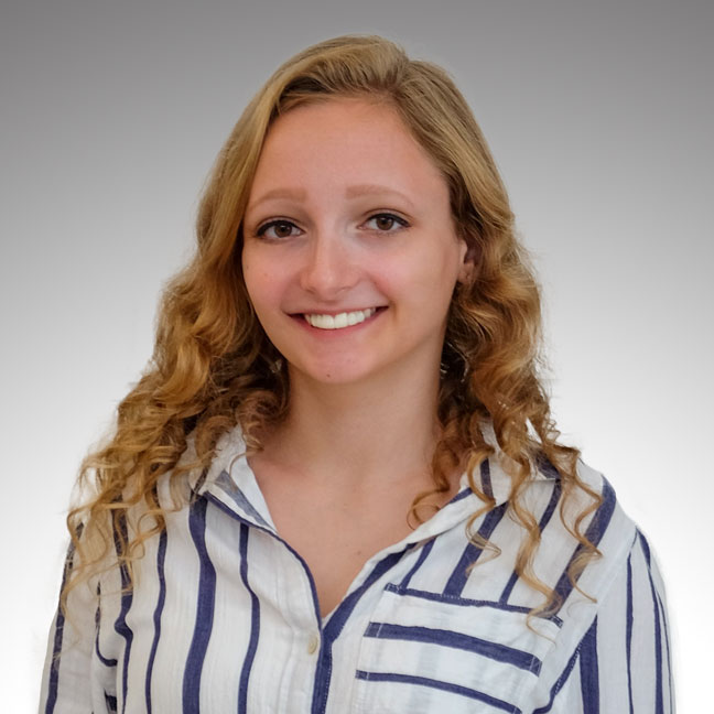 Nicole Mester Portrait of a smiling person with curly hair, wearing a striped shirt.
