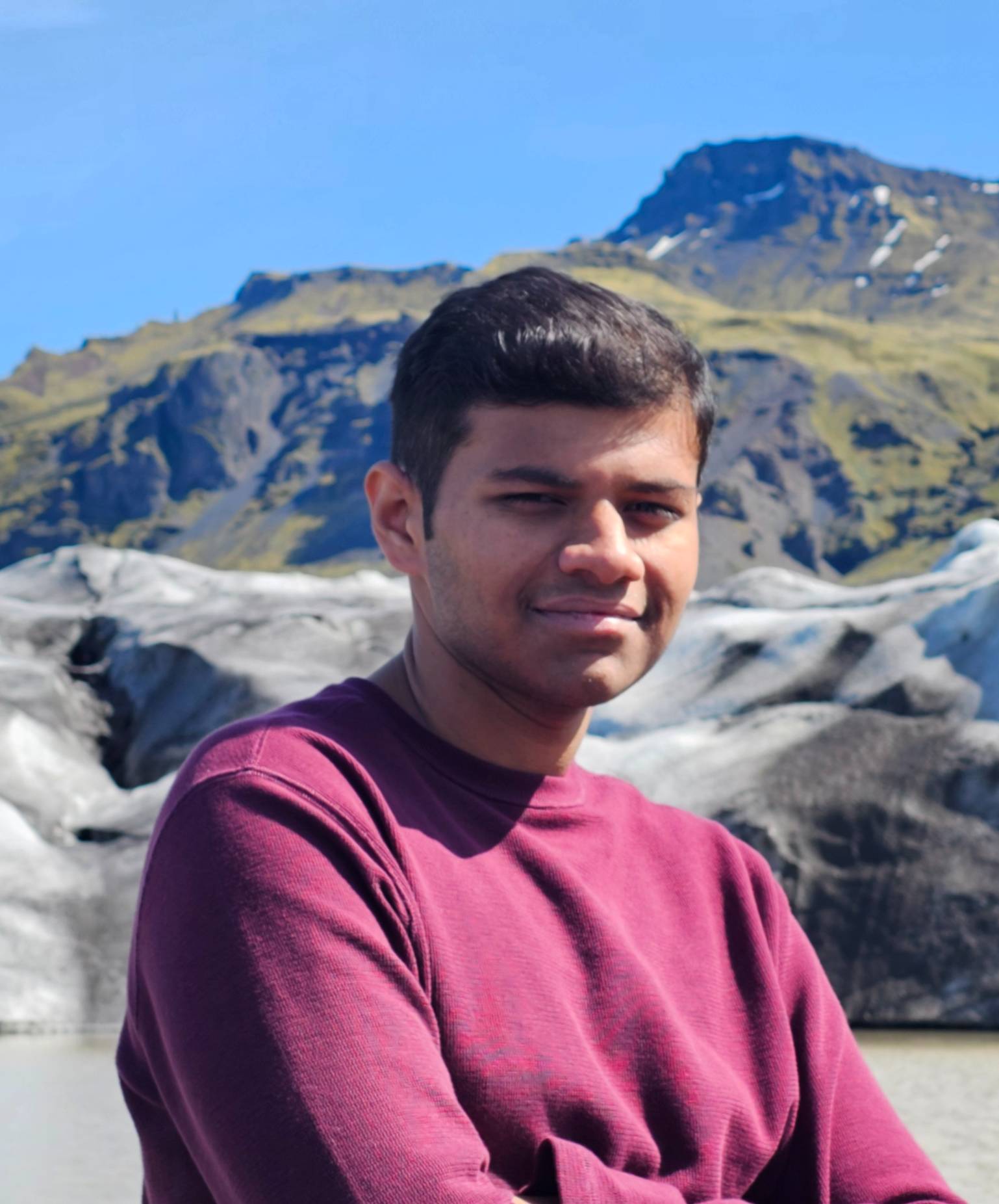 Shriram Hegde Person in a purple sweater smiling in front of a glacier and lake.