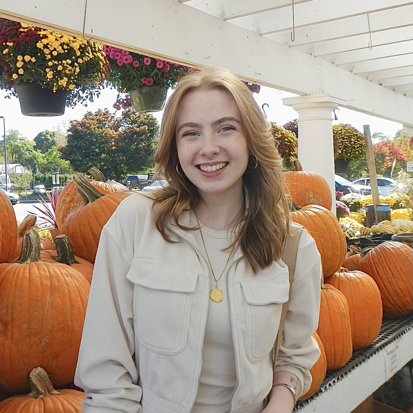 Person smiling at a pumpkin patch stand under a sunny sky.