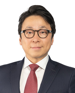 Portrait of a person wearing glasses, a navy suit, and a red patterned tie, set against a white background.