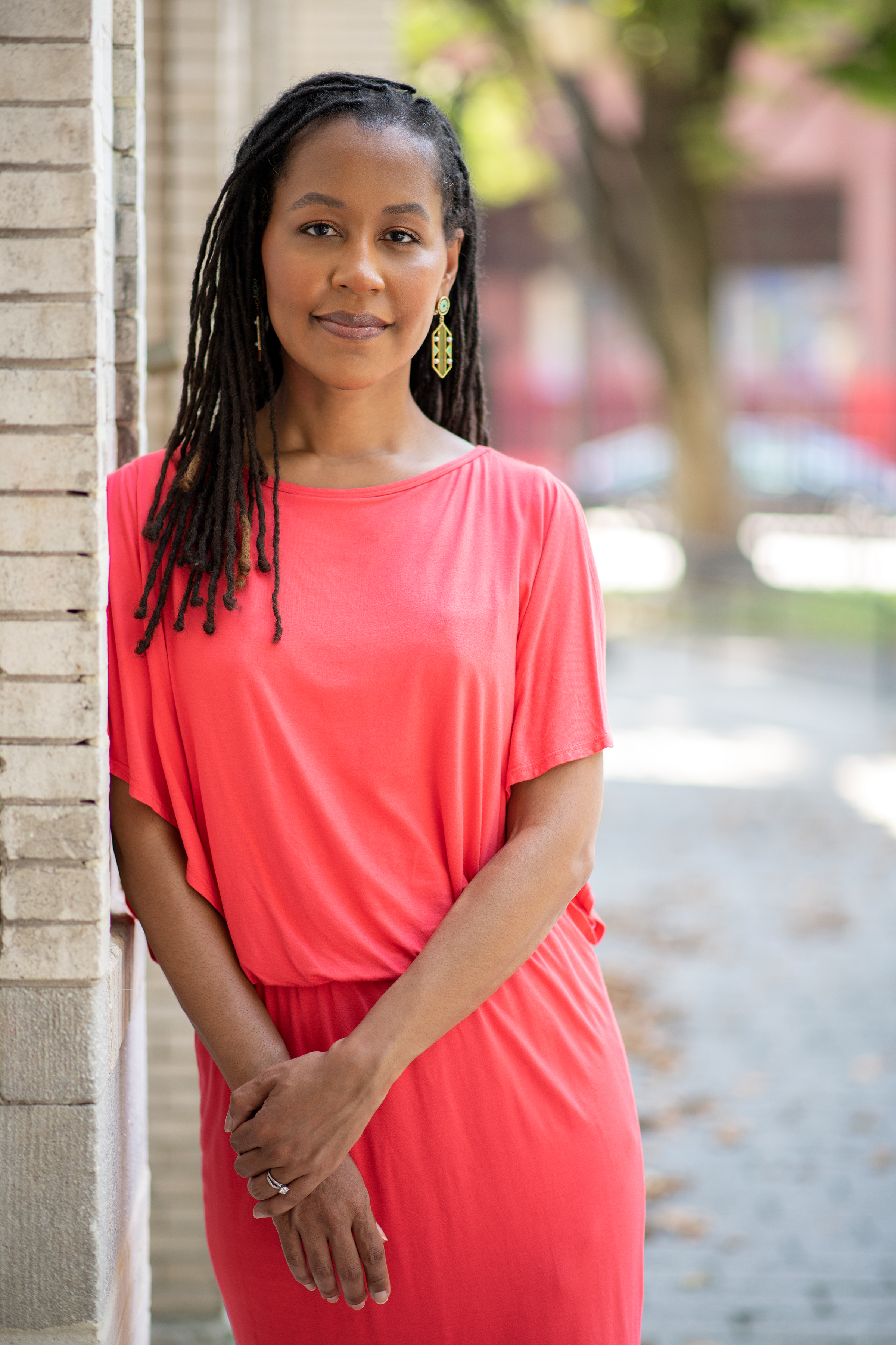 Individual in a bright pink dress standing beside a brick wall, smiling at the camera.