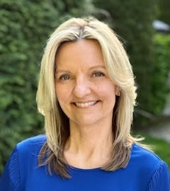 Portrait of an individual smiling, wearing a blue top, set against a blurred green background.