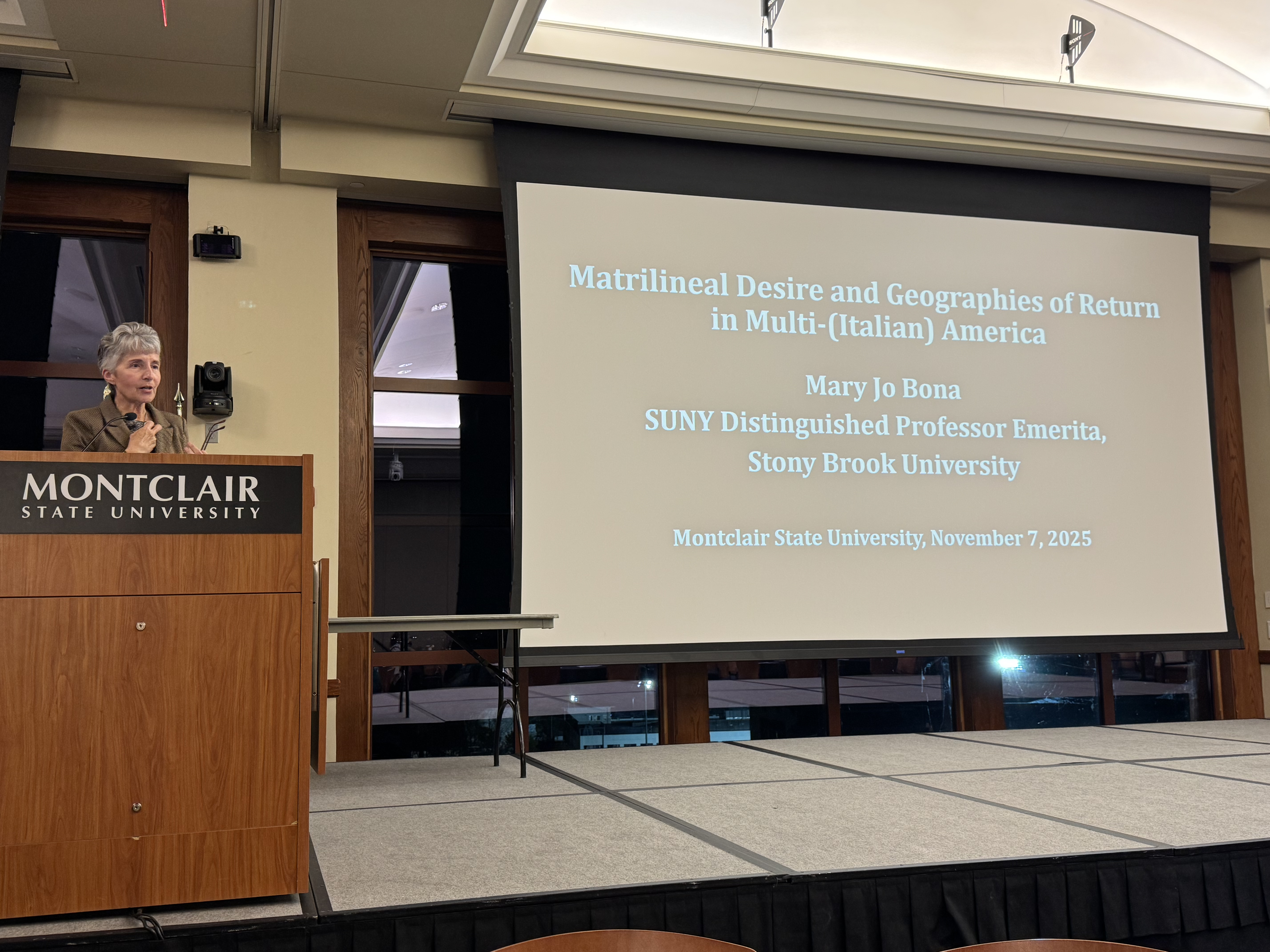 photo of Mary Jo Bona on stage, by a podium, presenting her presentation titled "Matrilineal Desire and Geographies of Return in America"