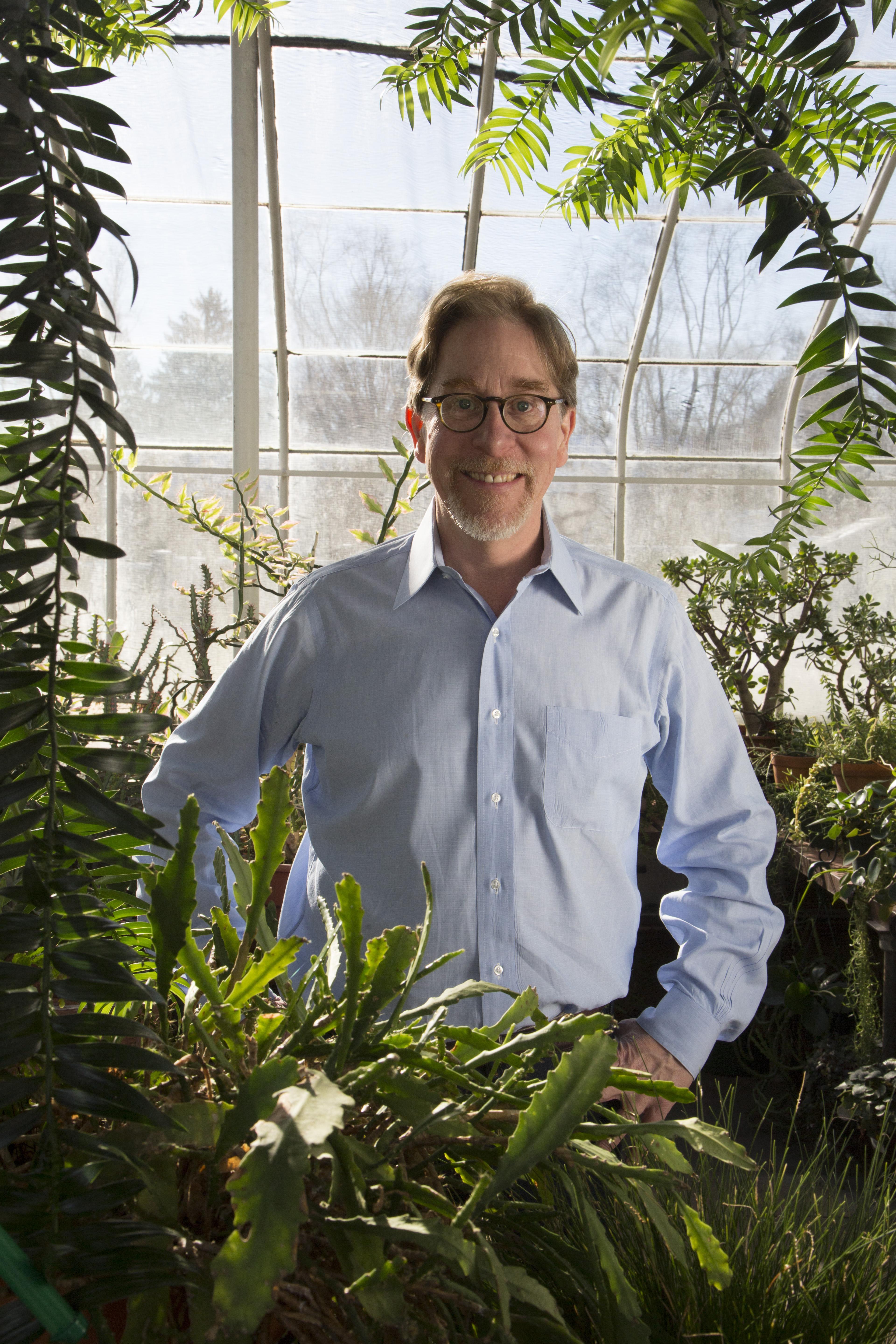 Richard Prums stands behind greenery wearing a blue button shirt