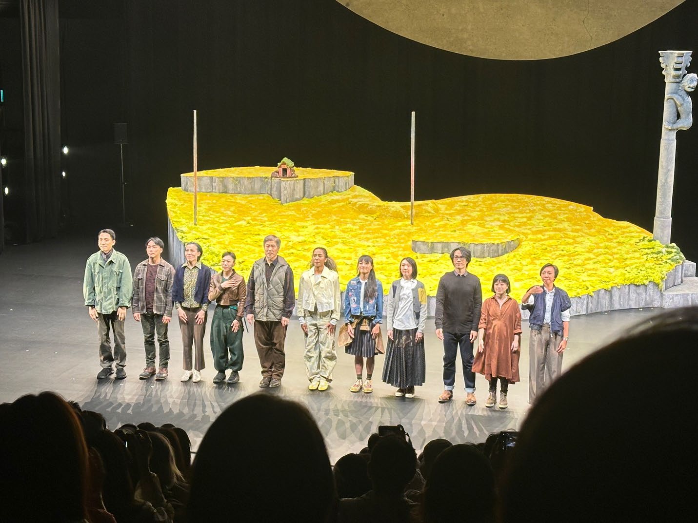 Hong Kong Theater Cast members of a theater production taking a bow on stage, featuring a set designed to look like a golden field under a large circular backdrop.